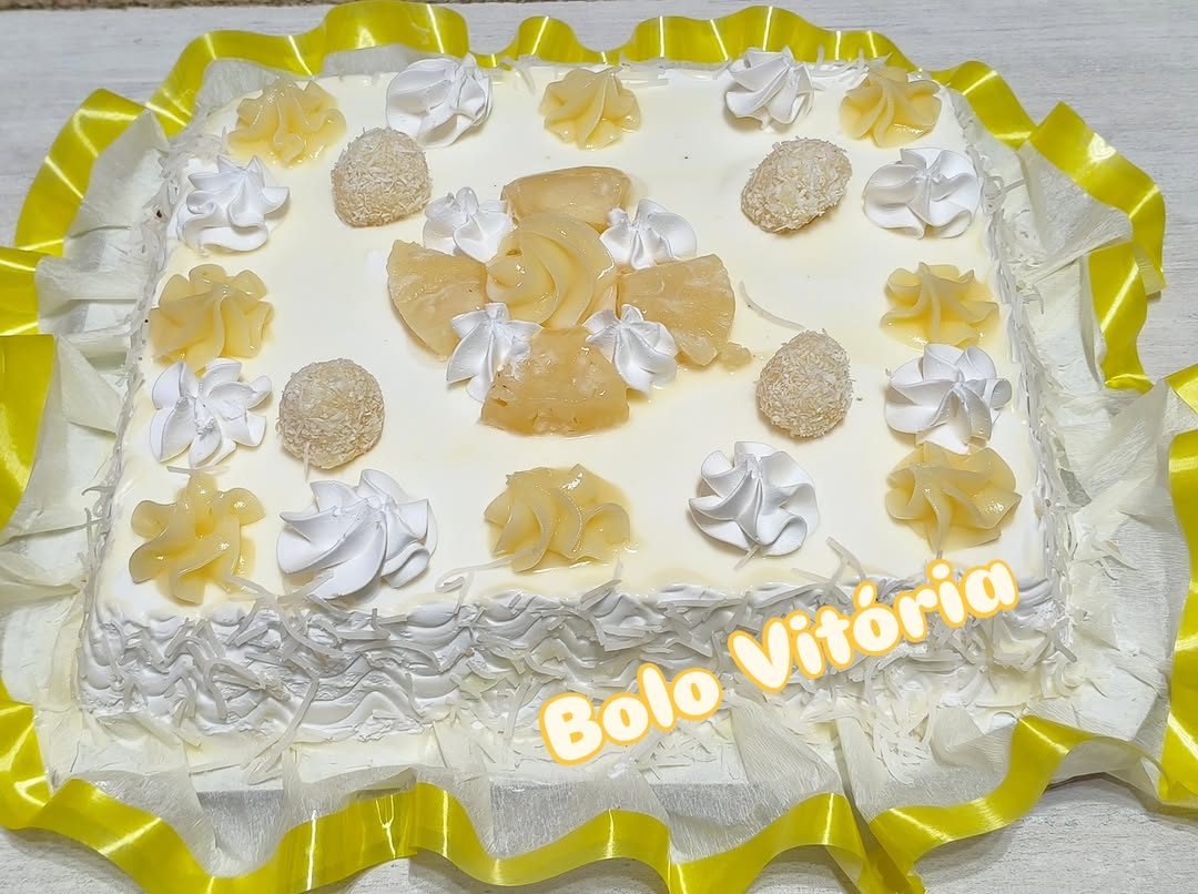 Bolo Vitória com cobertura branca, detalhes amarelos e docinhos sobre o bolo